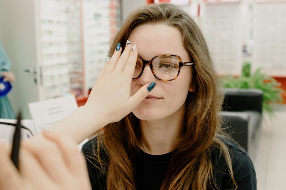 Focused female patient looking at hand of unrecognizable ophthalmologist while checking eyesight in new eyeglasses during appointment in clinic on blurred background